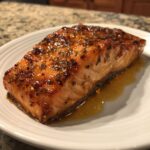 Close-up of a perfectly cooked, glazed salmon fillet resting in its sauce on a white plate.