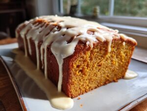 A close-up of a moist sweet potato pound cake loaf drizzled heavily with white vanilla glaze.