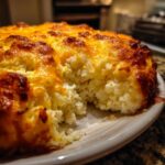 Close-up of cheesy baked mashed potatoes with a golden, bubbly crust, showing a scoop taken out.