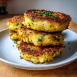 A stack of four golden brown, pan-fried mashed potato cakes garnished with fresh chives.