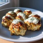 Close-up of golden brown Greek chicken meatballs topped with creamy yogurt sauce and fresh dill.