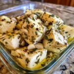 Cubes of white cheese soaking in olive oil with garlic cloves and herbs for marinated cheese.