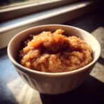 Close-up of chunky homemade applesauce, sprinkled with cinnamon, served in a white bowl.