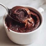 A spoonful of rich, dark homemade chocolate pudding being lifted from a white mug.