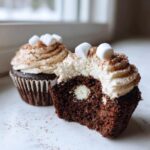 Close-up of a hot chocolate cupcake cut in half showing a white filling center, topped with cream frosting and mini marshmallows.