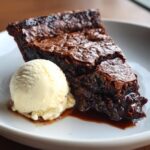 A decadent slice of hot fudge pie with a gooey center next to a scoop of melting vanilla ice cream.