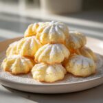 A tempting stack of freshly baked Italian butter cookies, lightly dusted with powdered sugar, sitting on a beige plate.