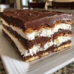 A cross-section view of a layered eclair cake showing graham cracker, vanilla cream, and chocolate pudding layers.