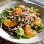 Close-up of a vibrant mandarin orange salad featuring bright citrus segments, feta cheese, red onion, and sliced almonds.