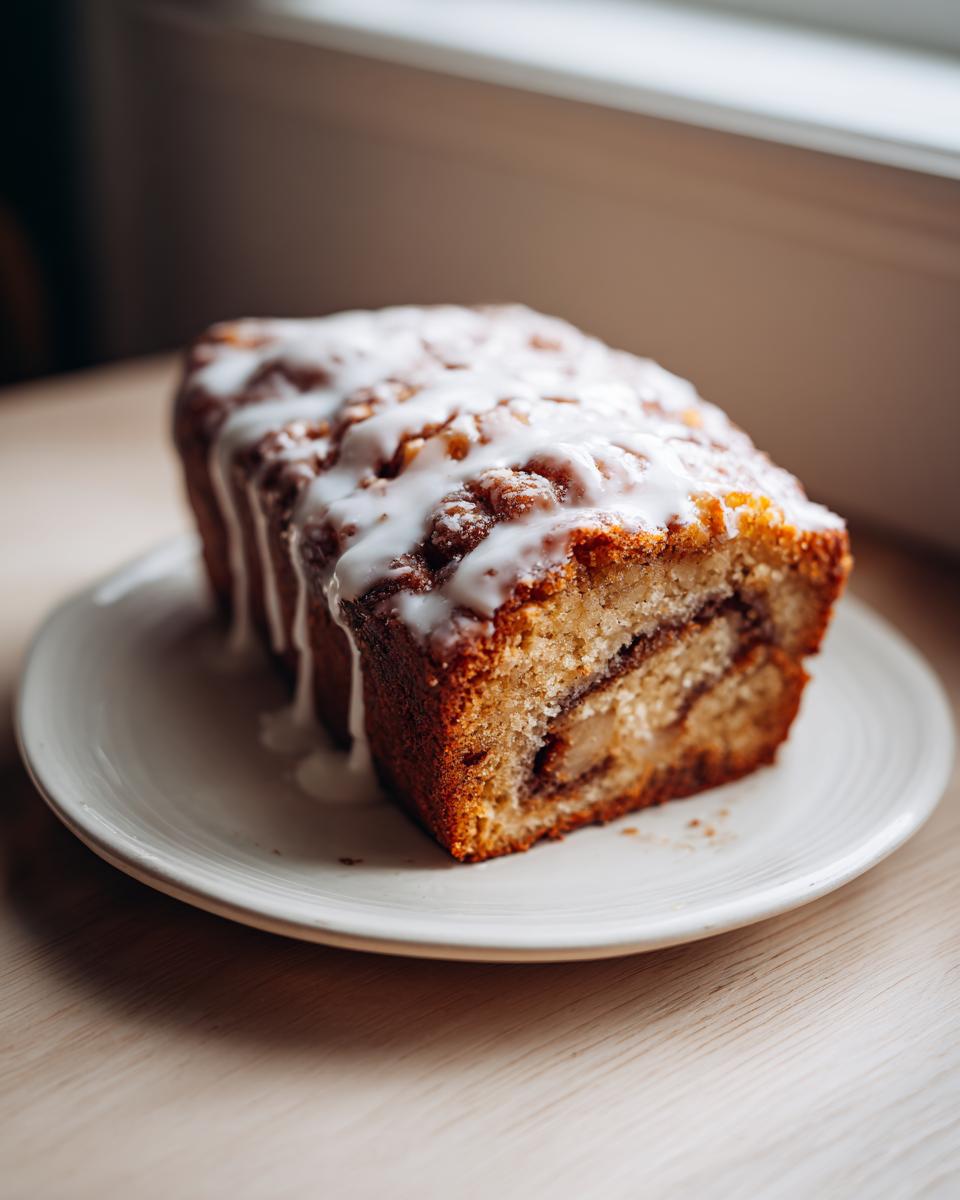 A loaf of moist apple fritter bread, sliced to show the interior, drizzled with white icing.