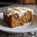 A close-up of a moist slice of applesauce cake topped with creamy vanilla frosting sprinkled with spices.