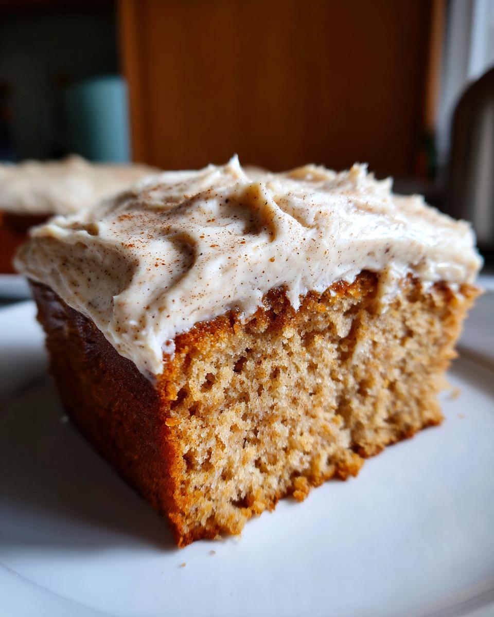 Close-up of a moist slice of applesauce cake topped with thick, spiced cream cheese frosting.
