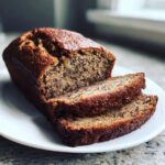 A loaf of freshly baked date nut bread, partially sliced, showing the moist interior texture and nuts.