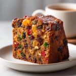 Close-up of a moist slice of fruit cake recipe packed with colorful candied and dried fruits.