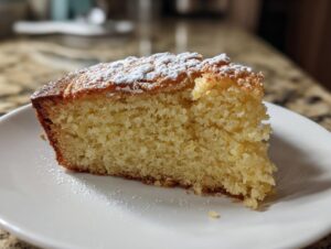 Close-up of a moist slice of yellow olive oil cake dusted with powdered sugar on a white plate.