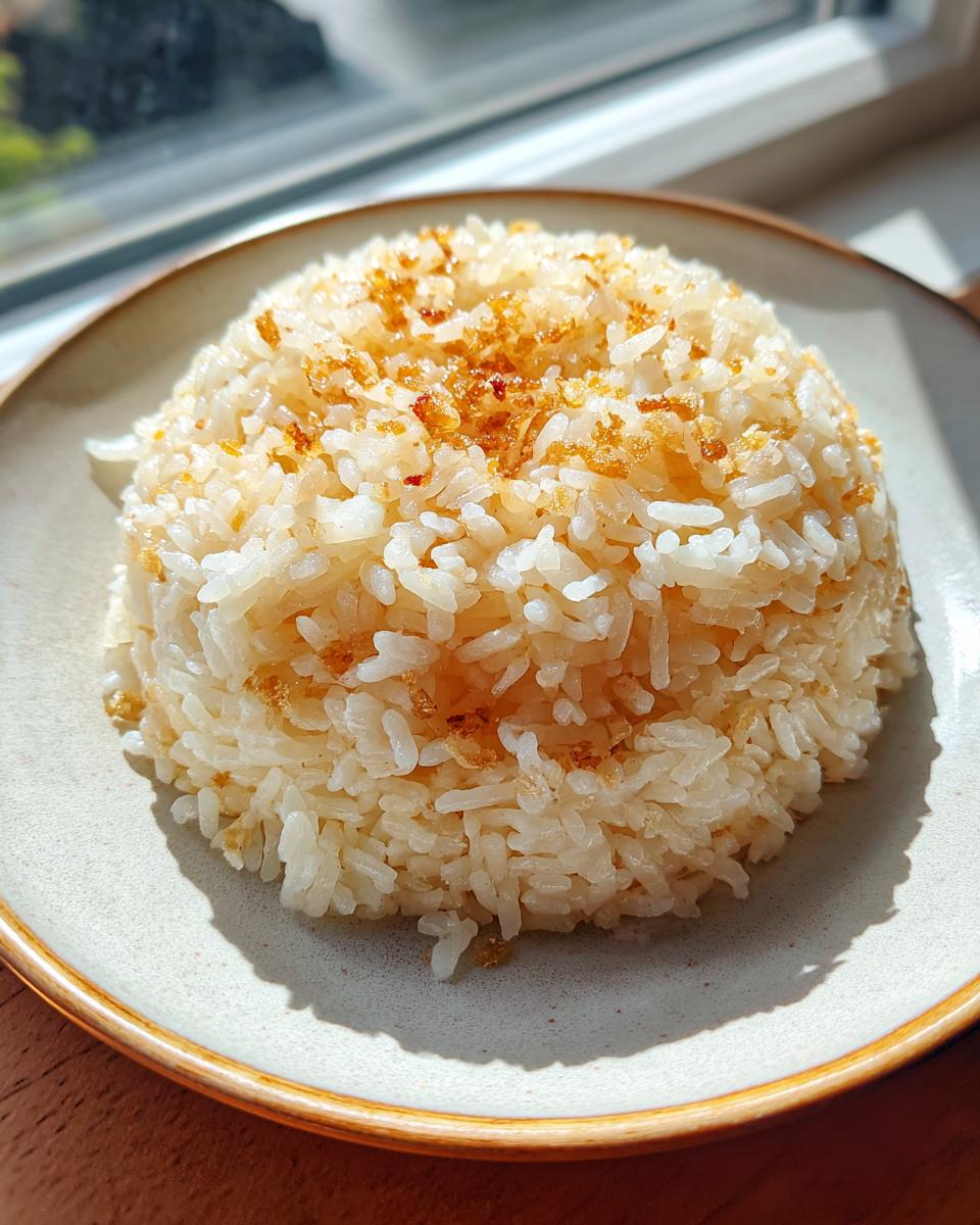 A mound of fluffy butter rice topped with golden brown crispy bits, served on a light-colored plate.