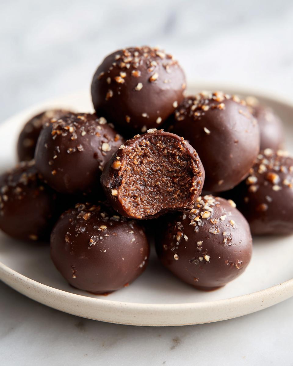 A stack of rich, chocolate-coated pecan pie balls, one with a bite taken out showing the dense interior.