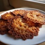 Close-up of several thin, lacy, golden-brown oatmeal lace cookies stacked on a white plate.