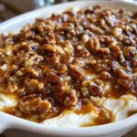 A close-up of a creamy white base topped generously with candied pecans in a rich caramel sauce, ready to serve as pecan pie dip.