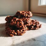 A close-up stack of rich, chocolatey no bake cookies made with oats, glistening in natural sunlight.