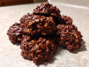 A close-up stack of rich, dark chocolate no bake cookies mixed with oats on a light countertop.