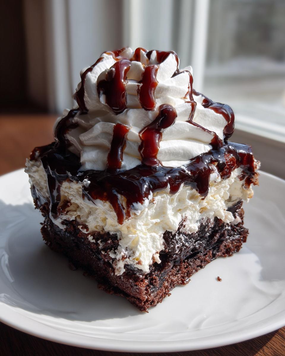 A decadent slice of chocolate poke cake topped with thick whipped cream and chocolate syrup drizzle.