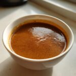 Close-up of rich, brown turkey gravy with a slight froth in a small white bowl.