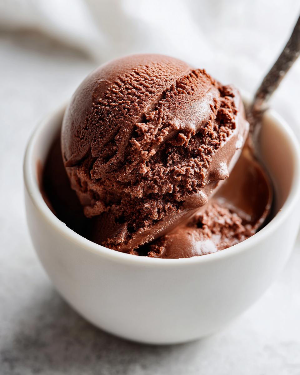 Close-up of a rich, dark scoop of homemade chocolate pudding served in a white bowl with a spoon.