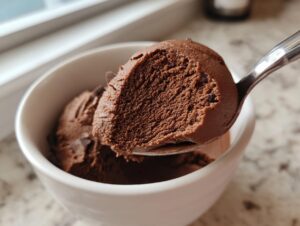 A spoonful of rich, dark homemade chocolate pudding being lifted from a white bowl.