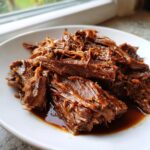 Close-up of tender, shredded Mississippi pot roast coated in rich brown gravy on a white plate.