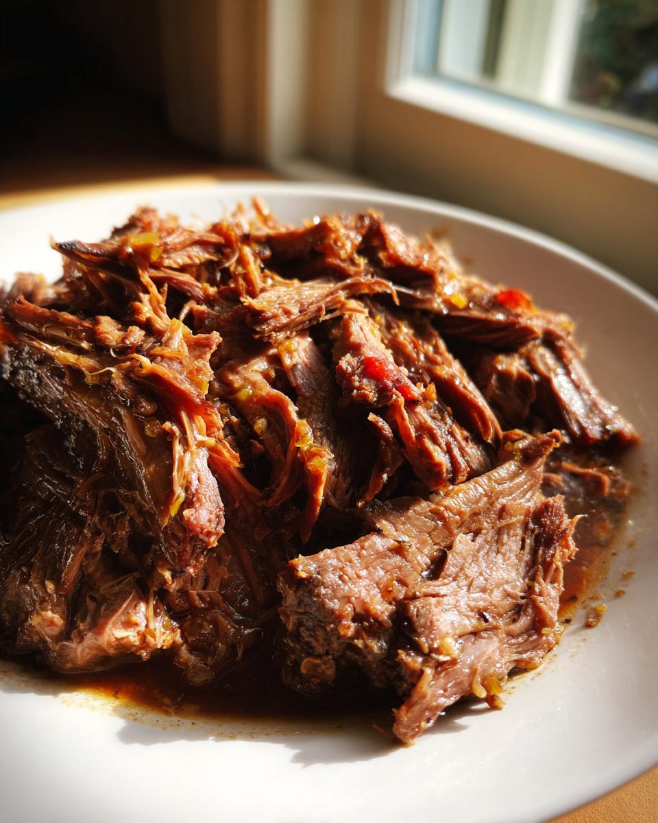 Close-up of tender, shredded Mississippi pot roast glistening with savory juices on a white plate.