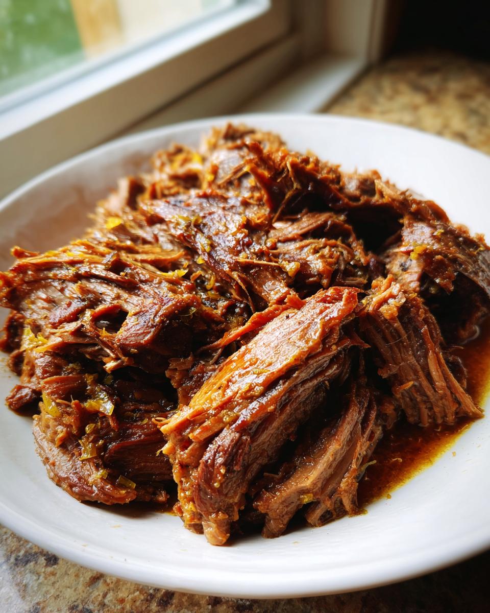 Close-up of tender, shredded Mississippi pot roast piled high on a white plate with rich brown juices.