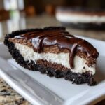 A decadent slice of 4-layer mud pie showing a dark crust, chocolate layer, white cream layer, and rich chocolate glaze topping.