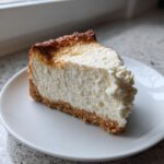 A close-up shot of a thick slice of baked Protein Cheesecake with a creamy white interior and a slightly browned top.