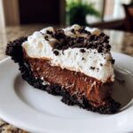 Close-up of a decadent slice of chocolate mousse pie featuring a dark crust, thick chocolate filling, and whipped cream topping.
