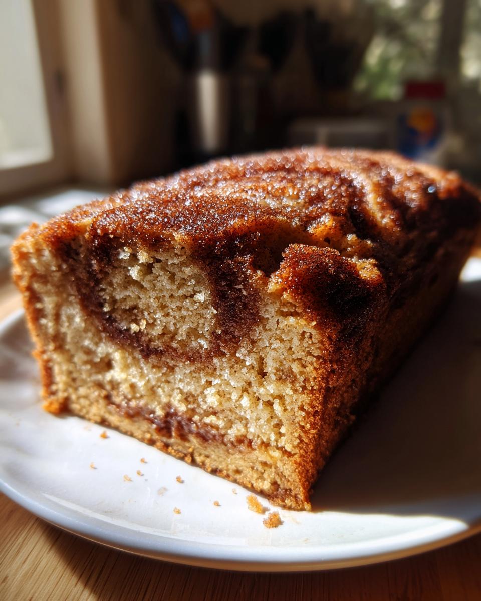 A slice of snickerdoodle banana bread with a cinnamon swirl topping, sitting on a white plate.