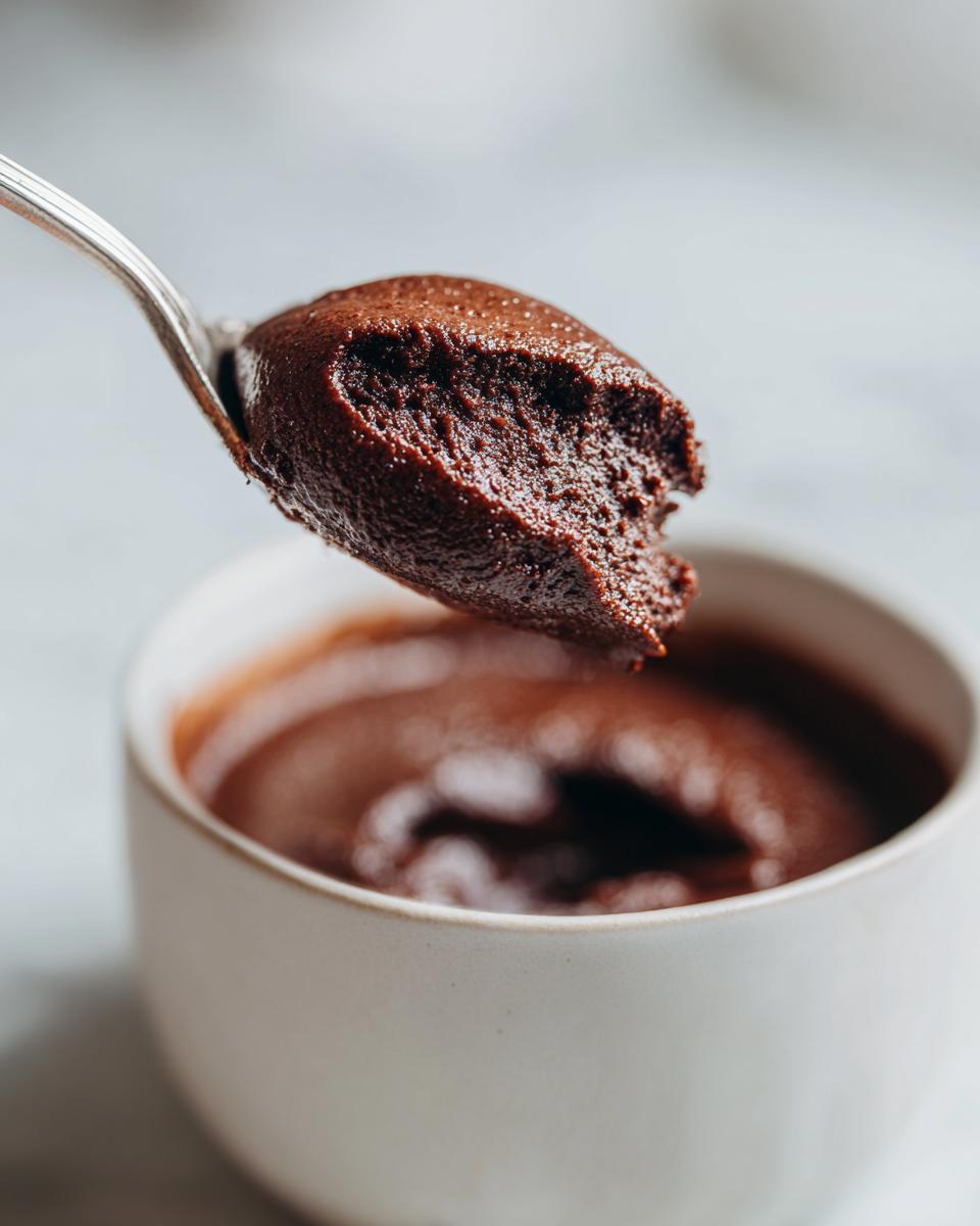 A close-up of a spoonful of rich, dark homemade chocolate pudding being lifted from a white ramekin.
