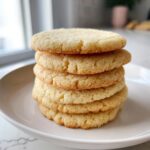 A stack of five perfectly baked, round sugar cookies resting on a white plate.