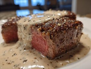 Close-up of a medium-rare steak generously covered in creamy peppercorn sauce.