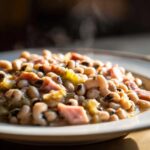 Close-up of a steaming bowl of savory black eyed peas recipe mixed with chunks of ham and celery.