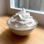 A small glass bowl filled with stiff, bright white royal icing recipe mixture, piped into a peak.