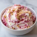 A white bowl filled with creamy, swirled strawberry cheesecake dip, topped with graham cracker crumbs.
