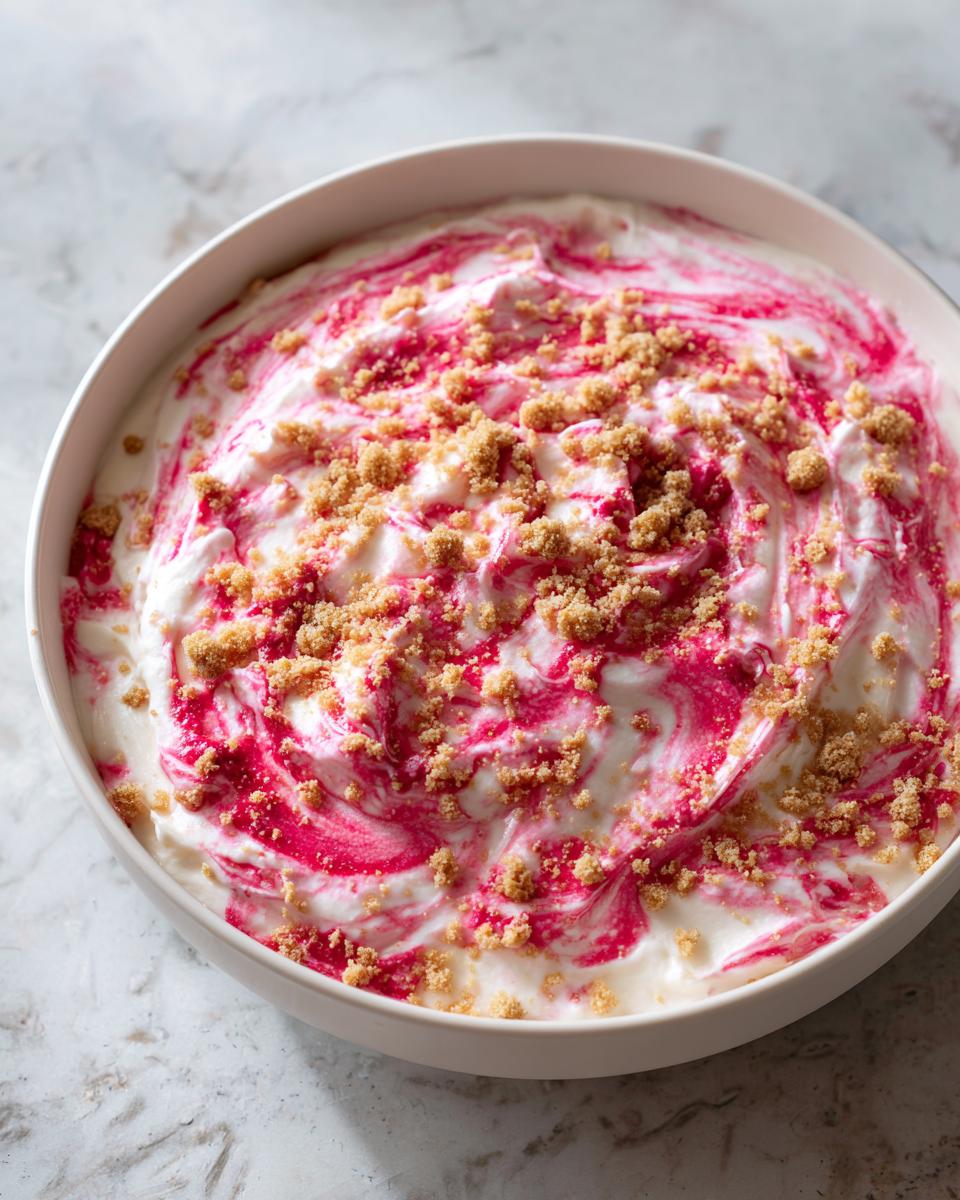 Close-up of finished strawberry cheesecake dip swirled with pink sauce and topped with graham cracker crumbs.