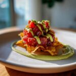 Close-up of vibrant tuna tartare stacked on crispy wonton chips, drizzled with avocado cream sauce.