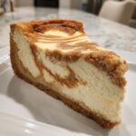 A close-up of a rich slice of sugar cookie cheesecake with a marbled brown and white swirl topping on a white plate.