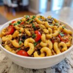 A white bowl filled with vibrant taco pasta salad featuring elbow macaroni, seasoned ground meat, cherry tomatoes, and black olives.
