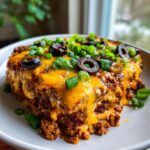A hearty, cheesy slice of texas trash dip topped with melted cheddar, black olives, and green onions.