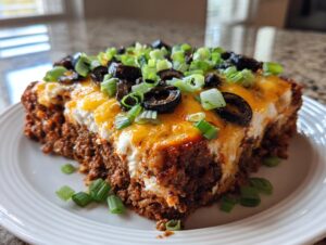 A thick slice of layered texas trash dip topped with melted cheese, black olives, and green onions.