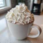 A mug of rich white hot chocolate generously topped with fluffy whipped cream.