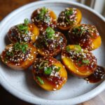 Halved, glossy marinated eggs coated in a dark glaze, topped with sesame seeds and chopped green onions.